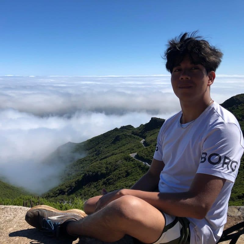 John sitting on a mountain above the clouds during a hike